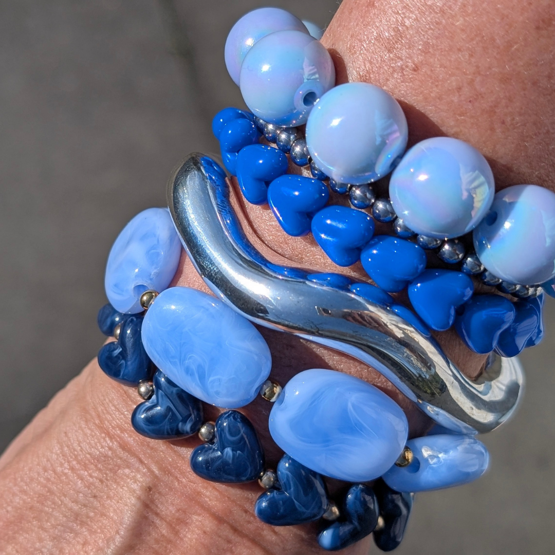 arm met donker blauwe marble hartjes armband, zilveren bangle, zilveren kraaltjes armband, platte lichtblauwe kralen en parelmoer ballen armband