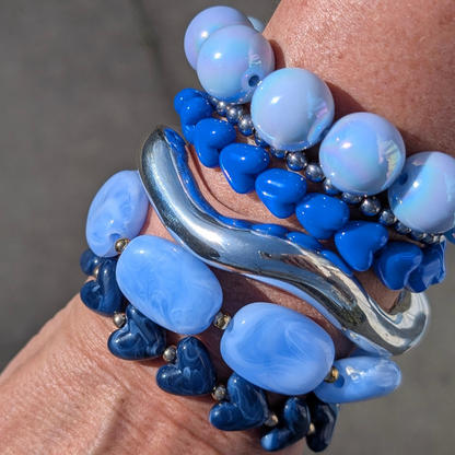 arm met donker blauwe marble hartjes armband, zilveren bangle, zilveren kraaltjes armband, platte lichtblauwe kralen en parelmoer ballen armband