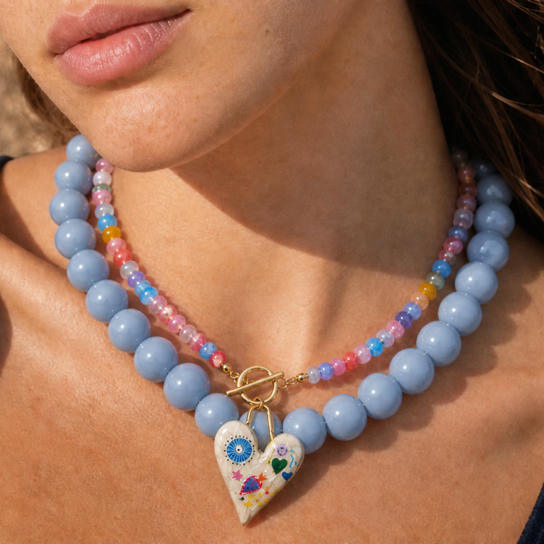Grote kralenketting en kleine glazen kralenketting met geschilderd hart gedragen.
