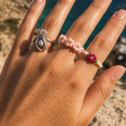 Hand met zilveren parelring en kleurrijke bloemenringen met roze, groene, witte en fuchsia kralen van Casa Jadel