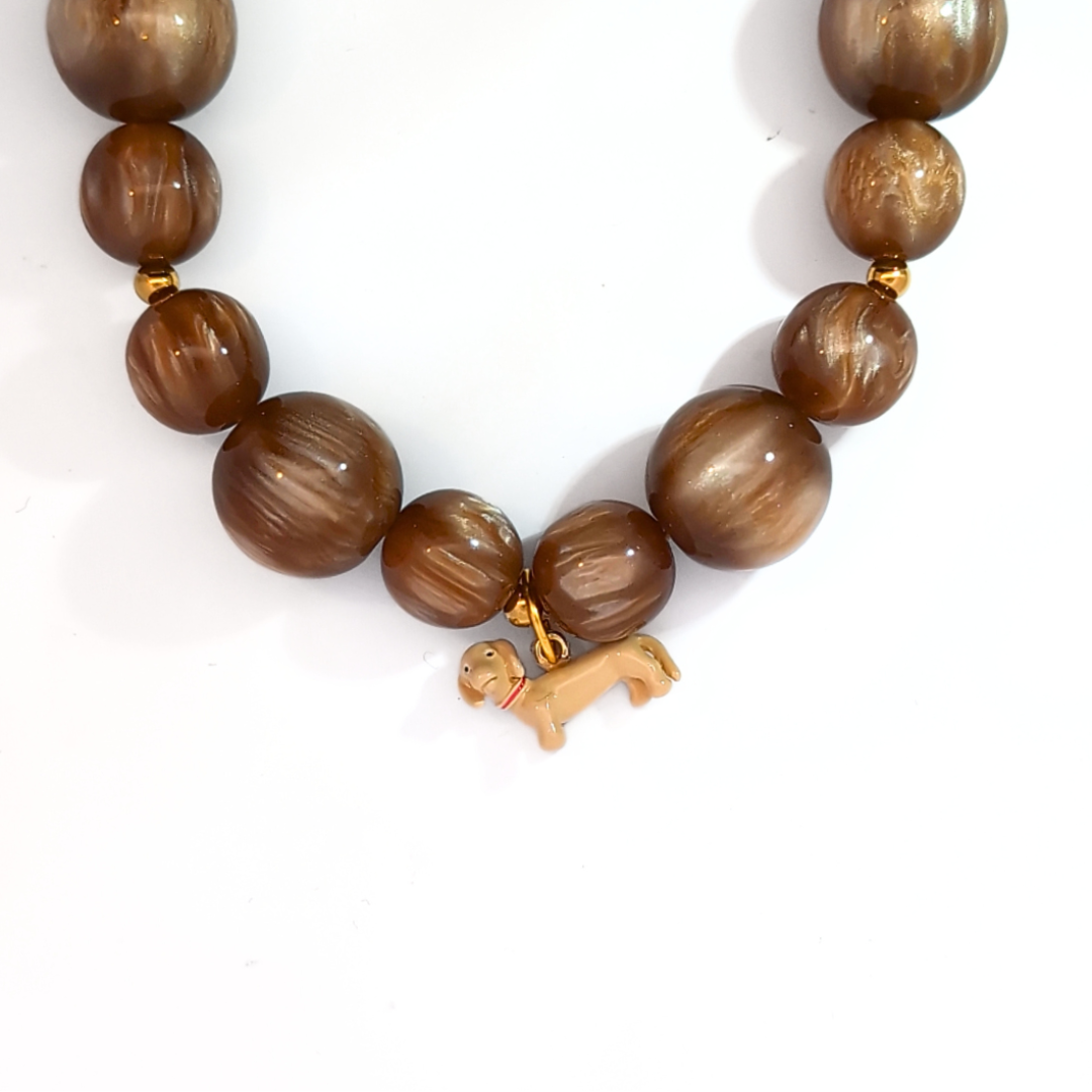 Blonde teckel hond bedel gedragen aan een groene kralenketting met goudkleurige sluiting
