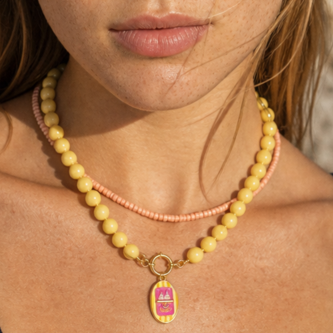 Model draagt een botergele kralenketting met roze kleine kralenketting en roze sardientjes bedel van Casa Jadel