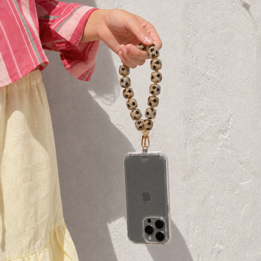 Model houdt telefoon vast met bruin gevlekt kralen telefoonkoord van Casa Jadel