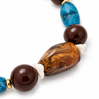 Detail van de amberbruine gemarmerde statement kraal van ketting The Lodge, met crèmekleurige accenten, bruine kralen en een turquoise facetkraal.