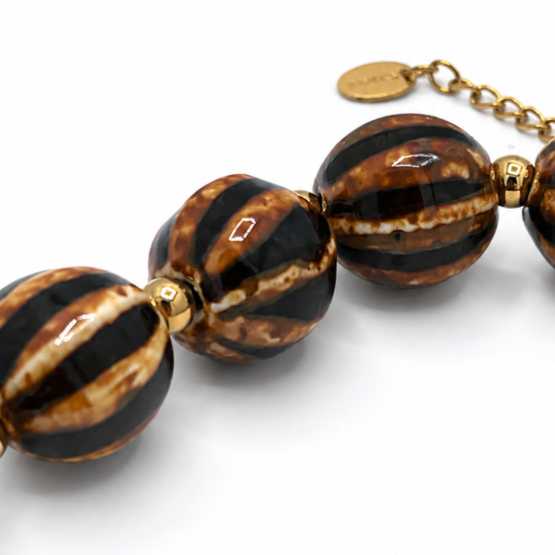 Close-up van bruine gestreepte kralenketting met goudkleurige sluiting van Casa Jadel
