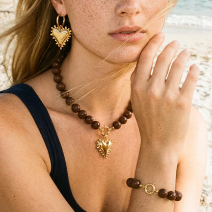 Bruine grote kralenketting met gouden hart bedel en bijpassende armband en oorbellen gedragen op het strand Casa Jadel