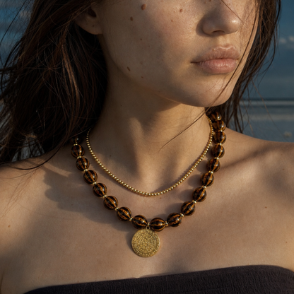 Model draagt bruine kralenketting met gouden munt bedel van Casa Jadel