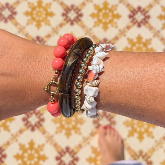 arm met bruine tube, schelpen armband en zalmroze kralenarmband 