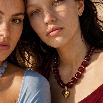 Model draagt een burgundy chunky kralenketting met goudkleurige details en gouden hartbedel van Casa Jadel