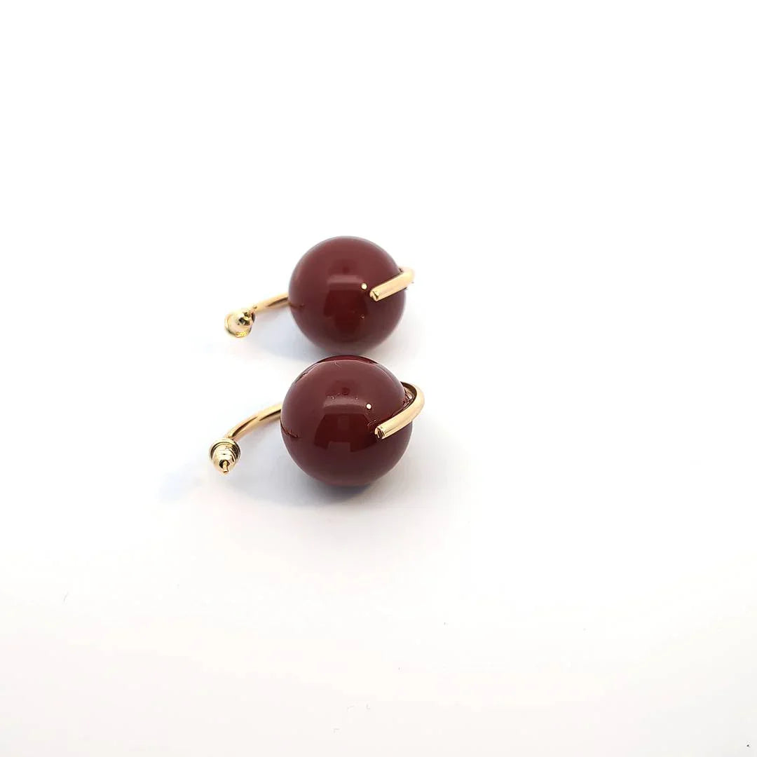 Burgundy statement oorringen met grote glanzende ronde donkerrode kralen en goudkleurige open gebogen oorringen draai