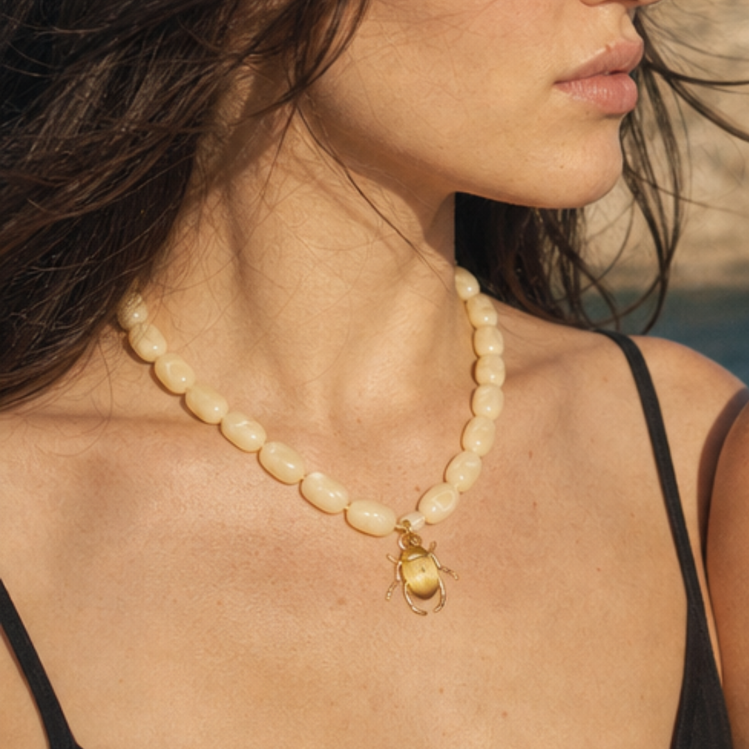 Model draagt een crèmekleurige kralenketting met goudkleurige keverbedel van Casa Jadel
