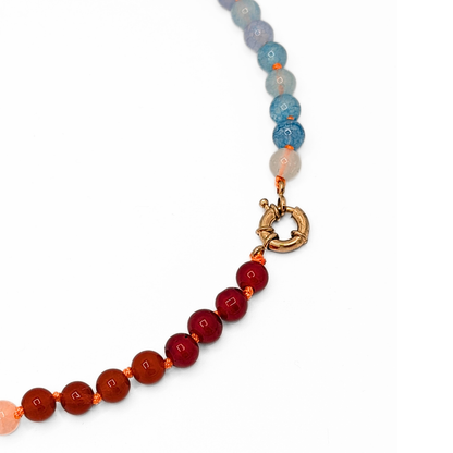 Detail van groen-blauwe glazen kralenketting met rood-oranje accenten en goudkleurig boeislot