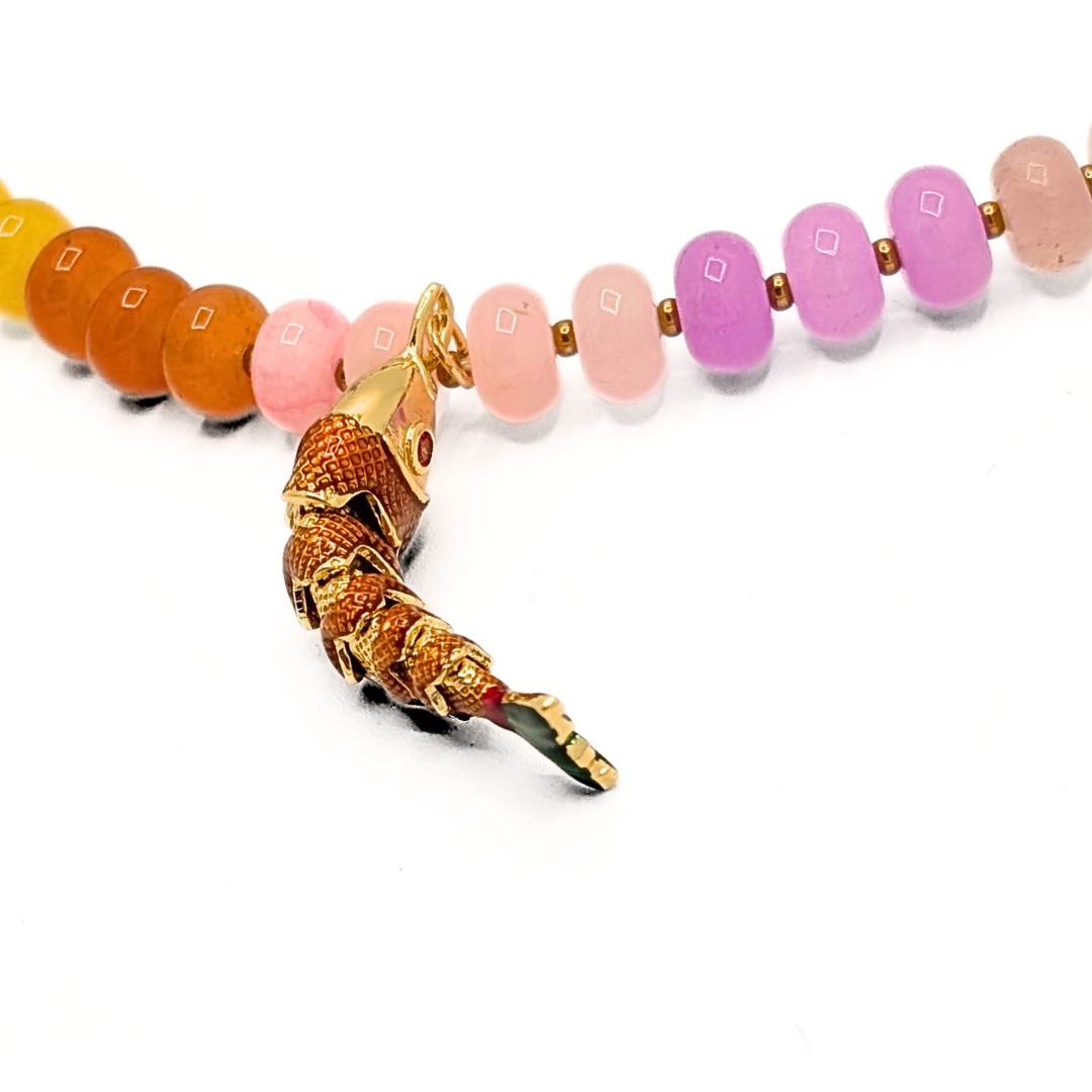 Detail van gebogen goudkleurige vis bedel aan kleurrijke kralenketting
