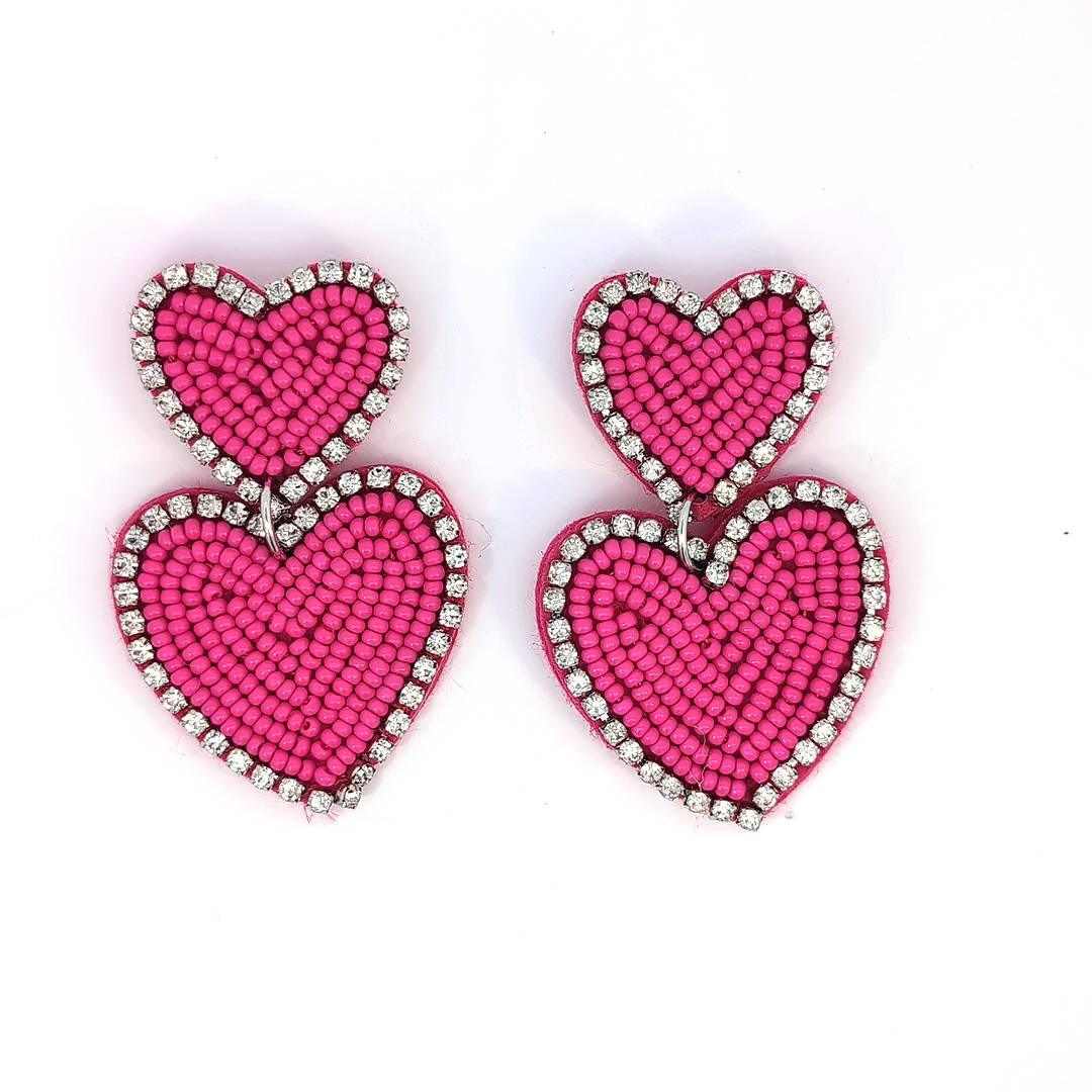 Felroze dubbele hart oorbellen met kraaltjes en strassrand op lichte achtergrond.