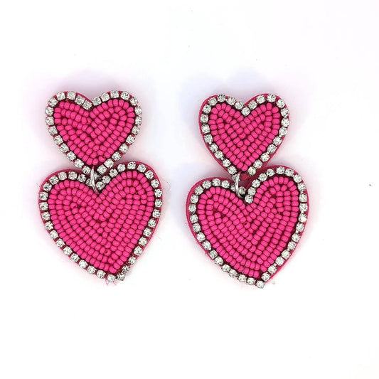 Felroze dubbele hart oorbellen met kraaltjes en strassrand op lichte achtergrond.