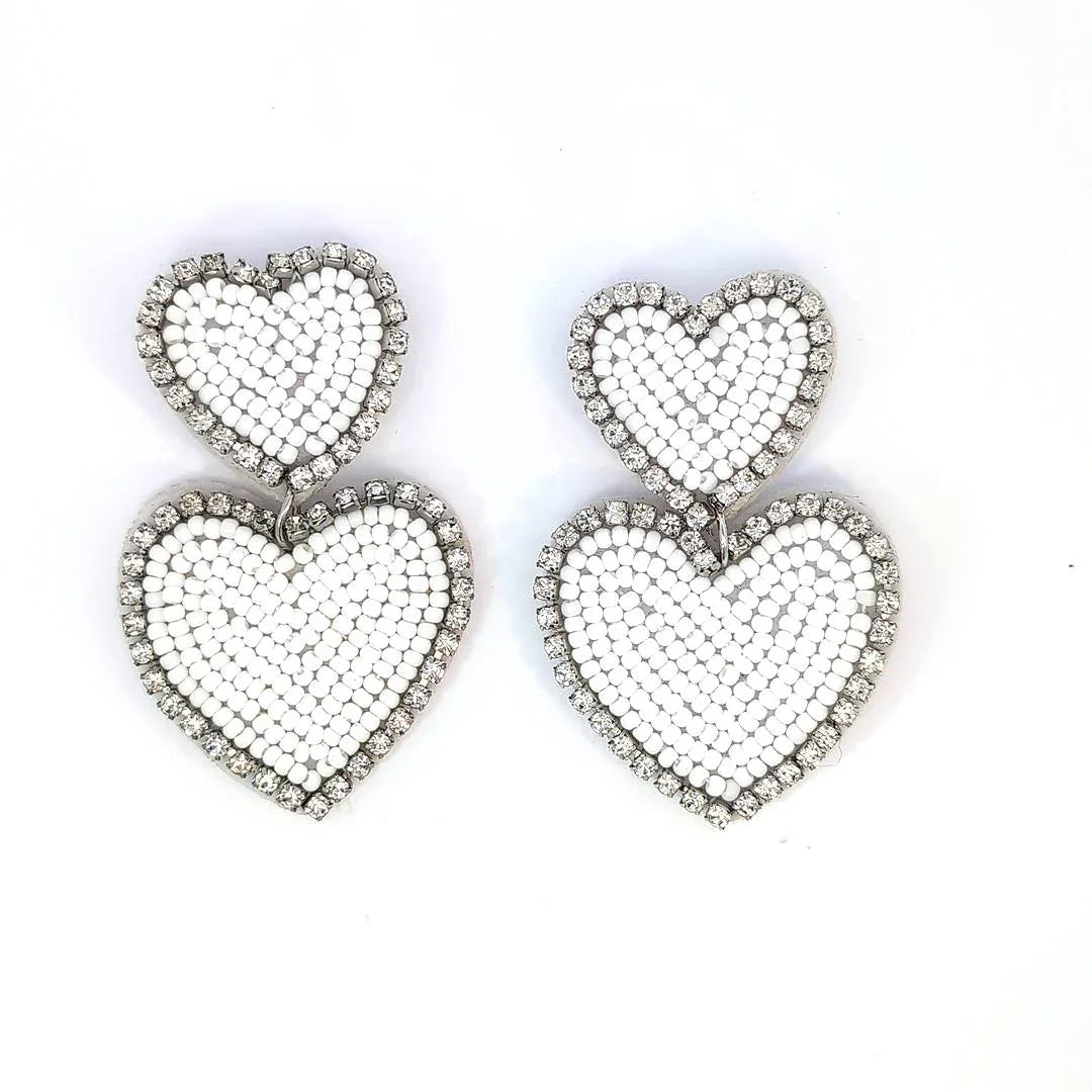 Witte dubbele hart oorbellen met kraaltjes en strassrand op lichte achtergrond.