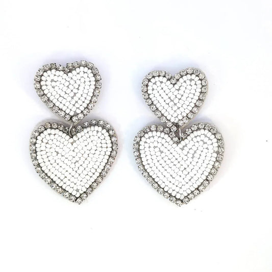 Witte dubbele hart oorbellen met kraaltjes en strassrand op lichte achtergrond.
