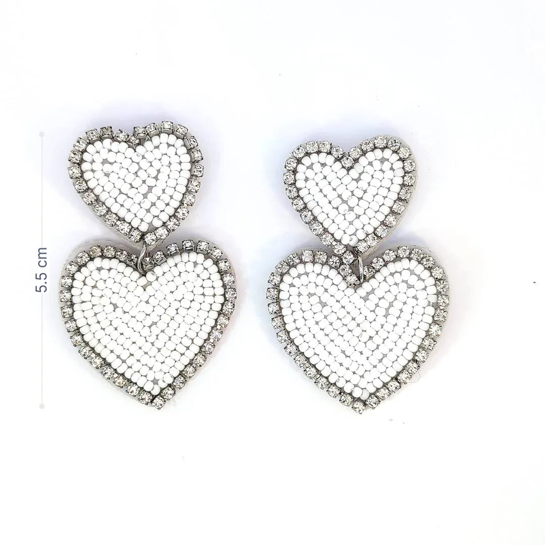 Witte dubbele hart oorbellen met kraaltjes en strassrand op lichte achtergrond. met afmeting
