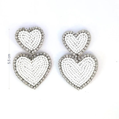 Witte dubbele hart oorbellen met kraaltjes en strassrand op lichte achtergrond. met afmeting