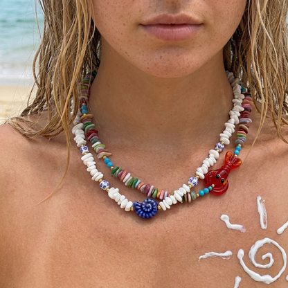 Model draagt dubbele kleurrijke kralenketting met schelpen en rode kreeft bedel van Casa Jadel