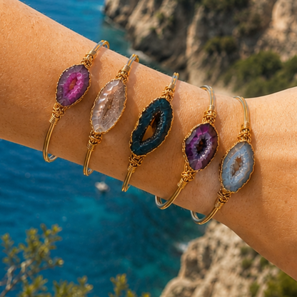 Arm met goudkleurige bangles met kleurrijke edelsteen details in roze, wit, blauw en paars van Casa Jadel