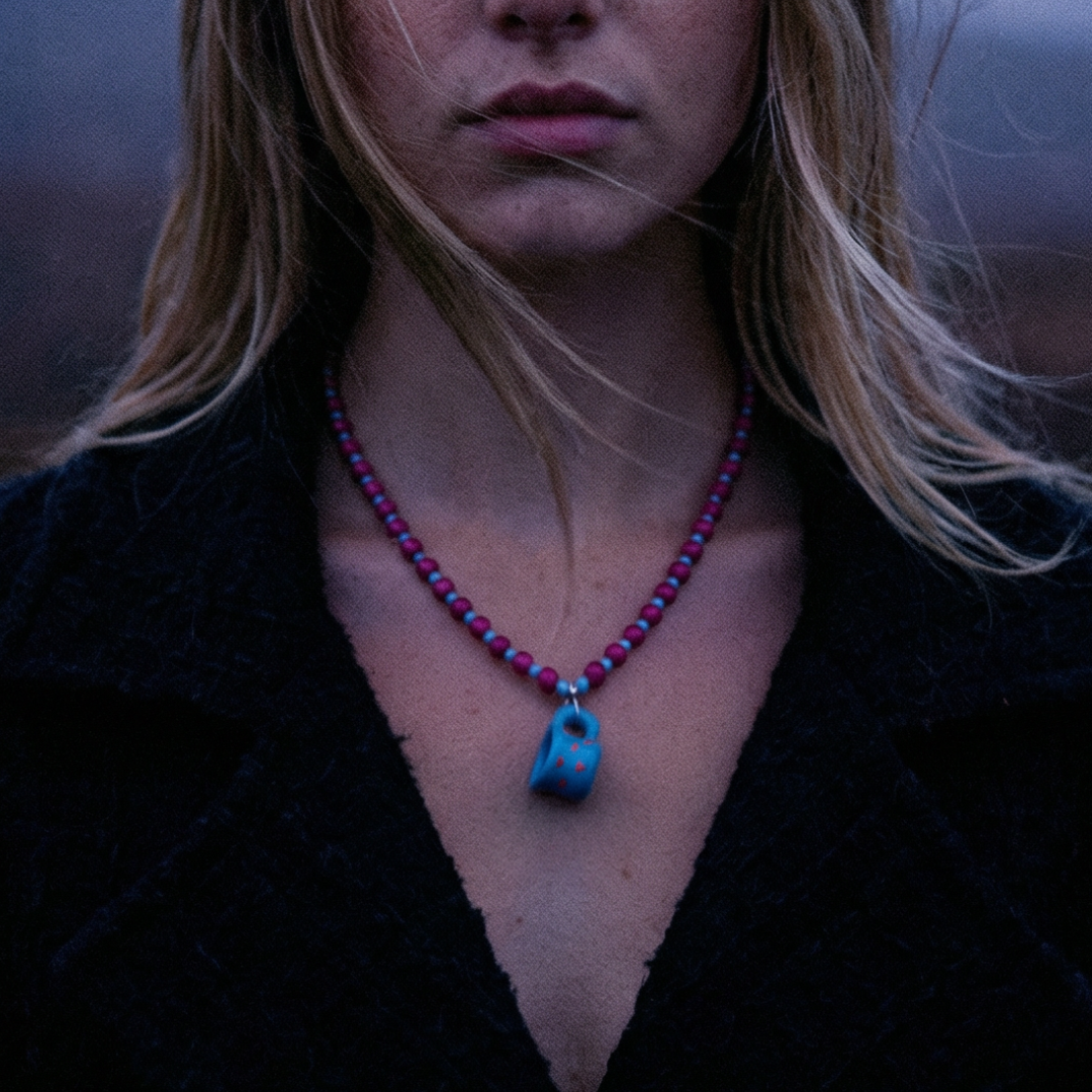 Fuchsia kralenketting met blauwe keramische bedel, gedragen in een donkere winterse setting – kleurrijke statement ketting met Ibiza vibe