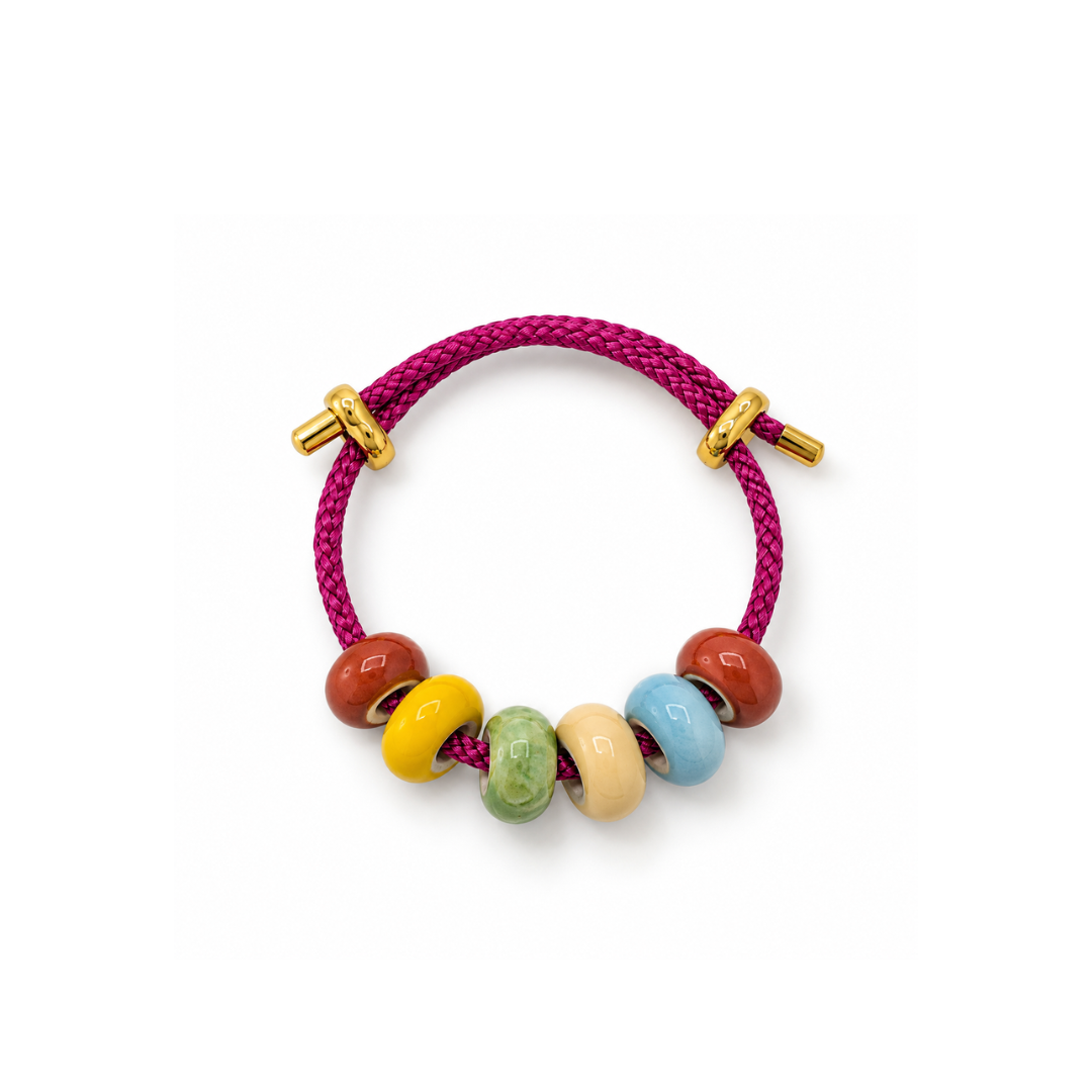 Fuchsia gevlochten rope armband met zes gekleurde keramiek kralen en goudkleurige schuifstukjes op een witte achtergrond.