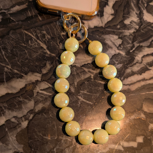 Gele facetgeslepen kralen telefoonkoord met glanzende ronde disco kralen en goudkleurige sluiting, gefotografeerd op een donkere marmeren ondergrond.