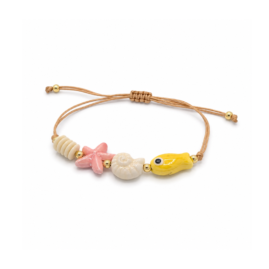 Verstelbaar rope armbandje met roze zeester, witte schelp, gele vis en goudkleurige details.