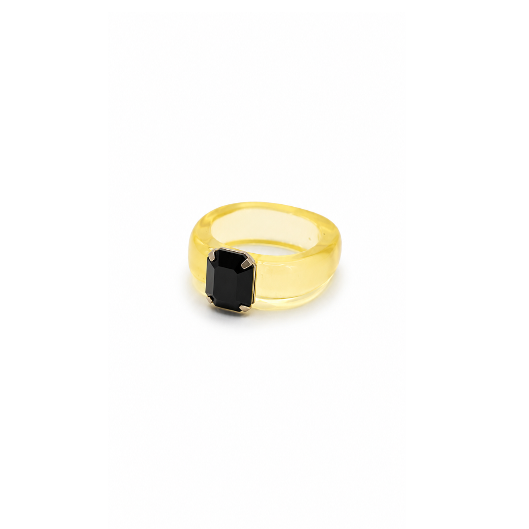Gele chunky ring in transparant geel met een rechthoekige zwarte steen op een witte achtergrond.