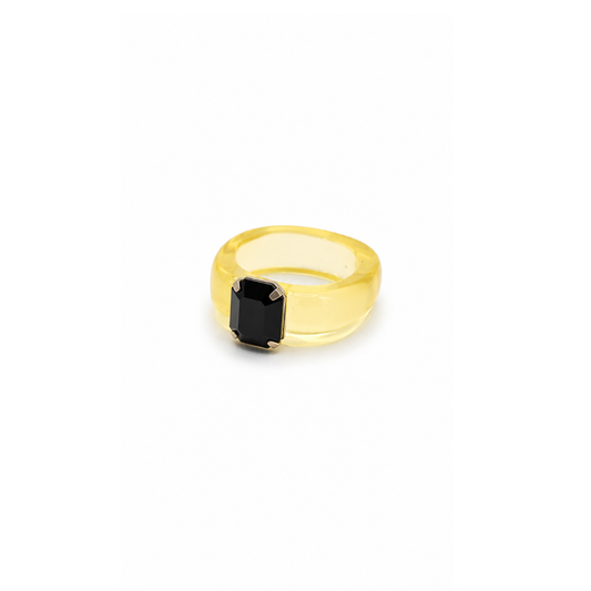 Gele chunky ring in transparant geel met een rechthoekige zwarte steen op een witte achtergrond.