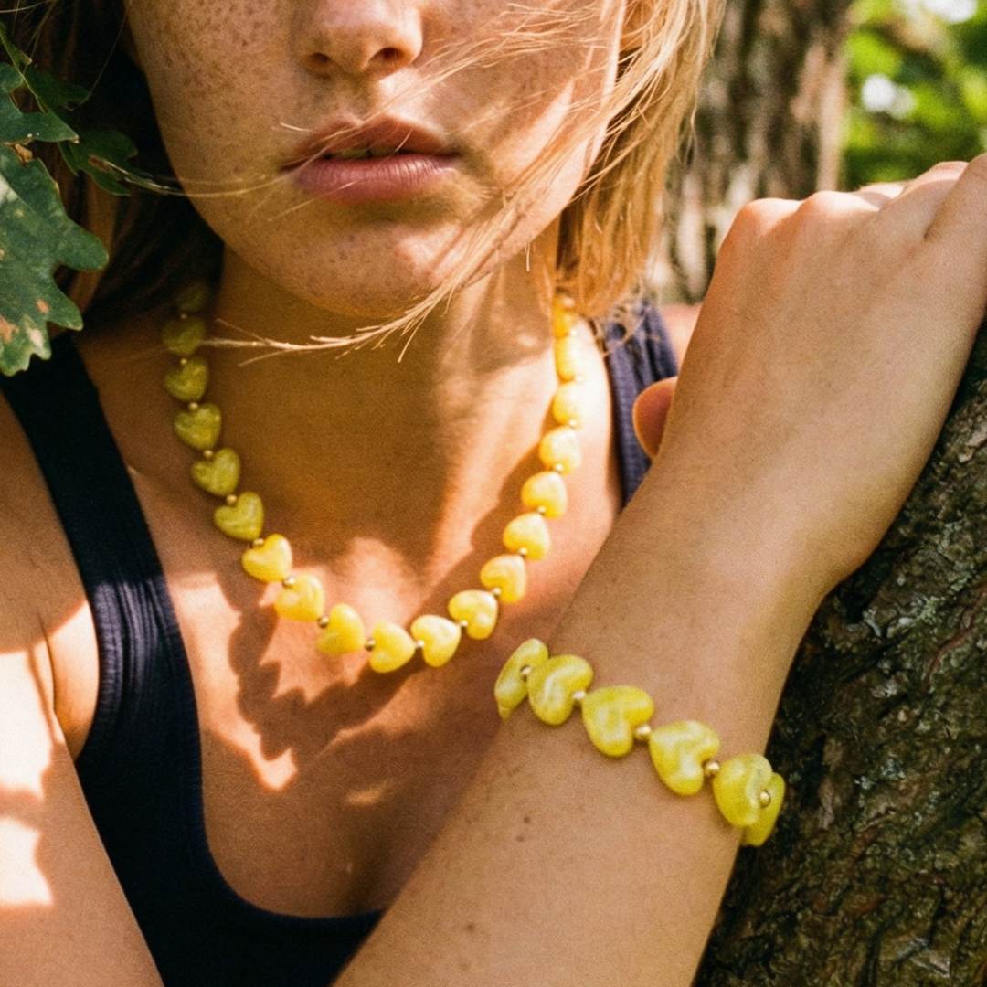 Gele hartjes kralenketting en bijpassende armband met gemarmerde hartvormige kralen, gedragen in een natuurlijke bosrijke setting – zomerse sieraden met Ibiza vibe