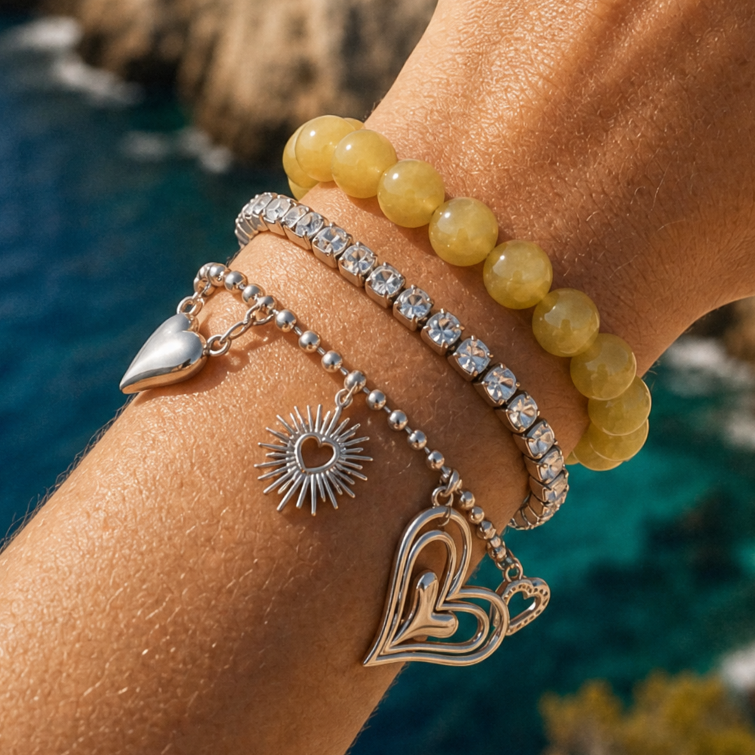Pols met gele kralenarmband en zilverkleurige armbanden met hart en zon bedels van Casa Jadel
