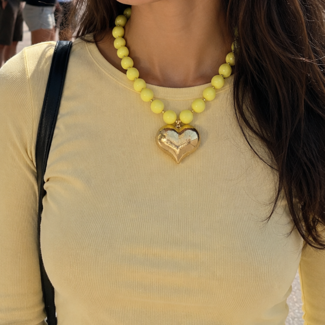 model met Gele kralenketting met grote gouden chubby hart bedel en goudkleurige details