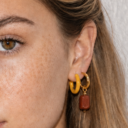 Close-up van model met gele oorring en goudkleurige oorring met bruine kraal bedel van Casa Jadel

