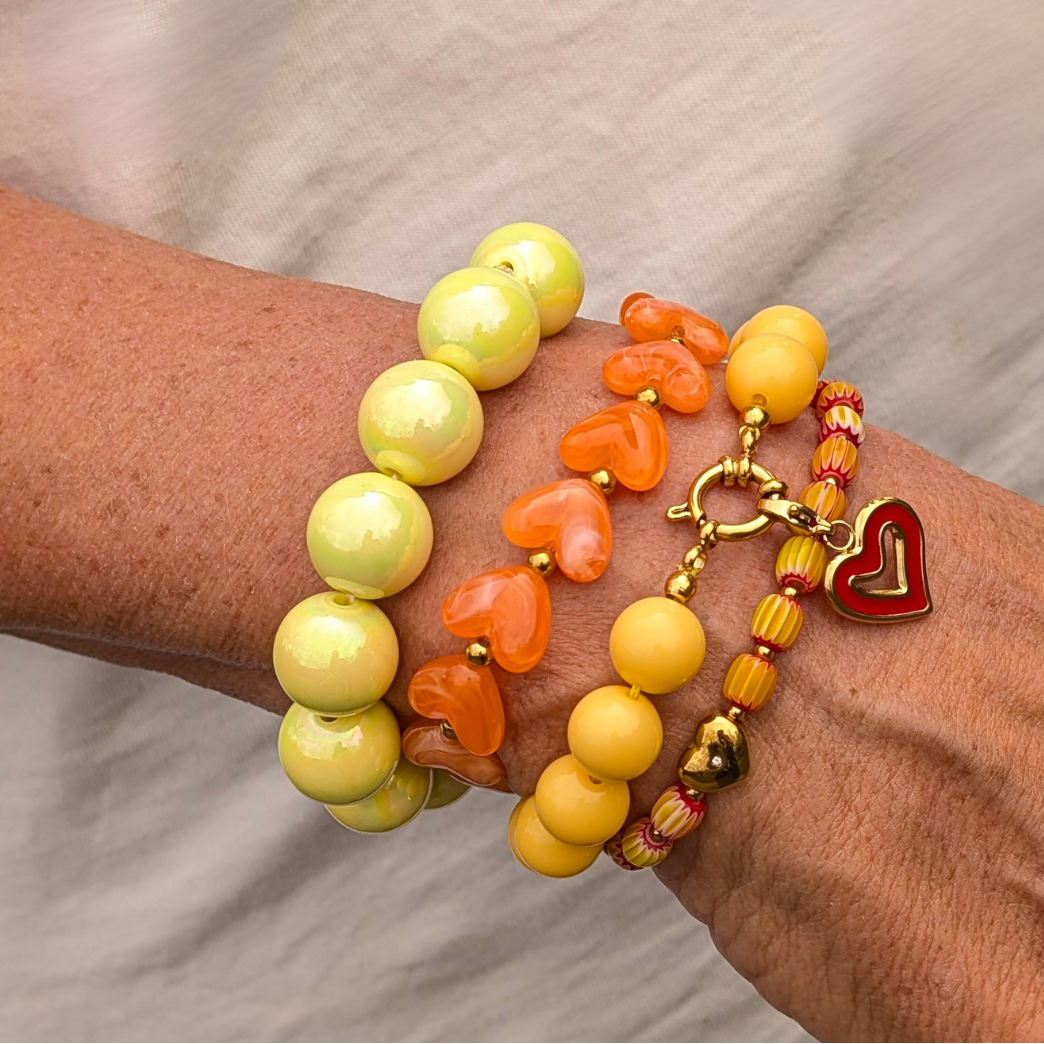 set gele en oranje kralenarmbanden met hartjes en gouden details om pols ibiza stijl