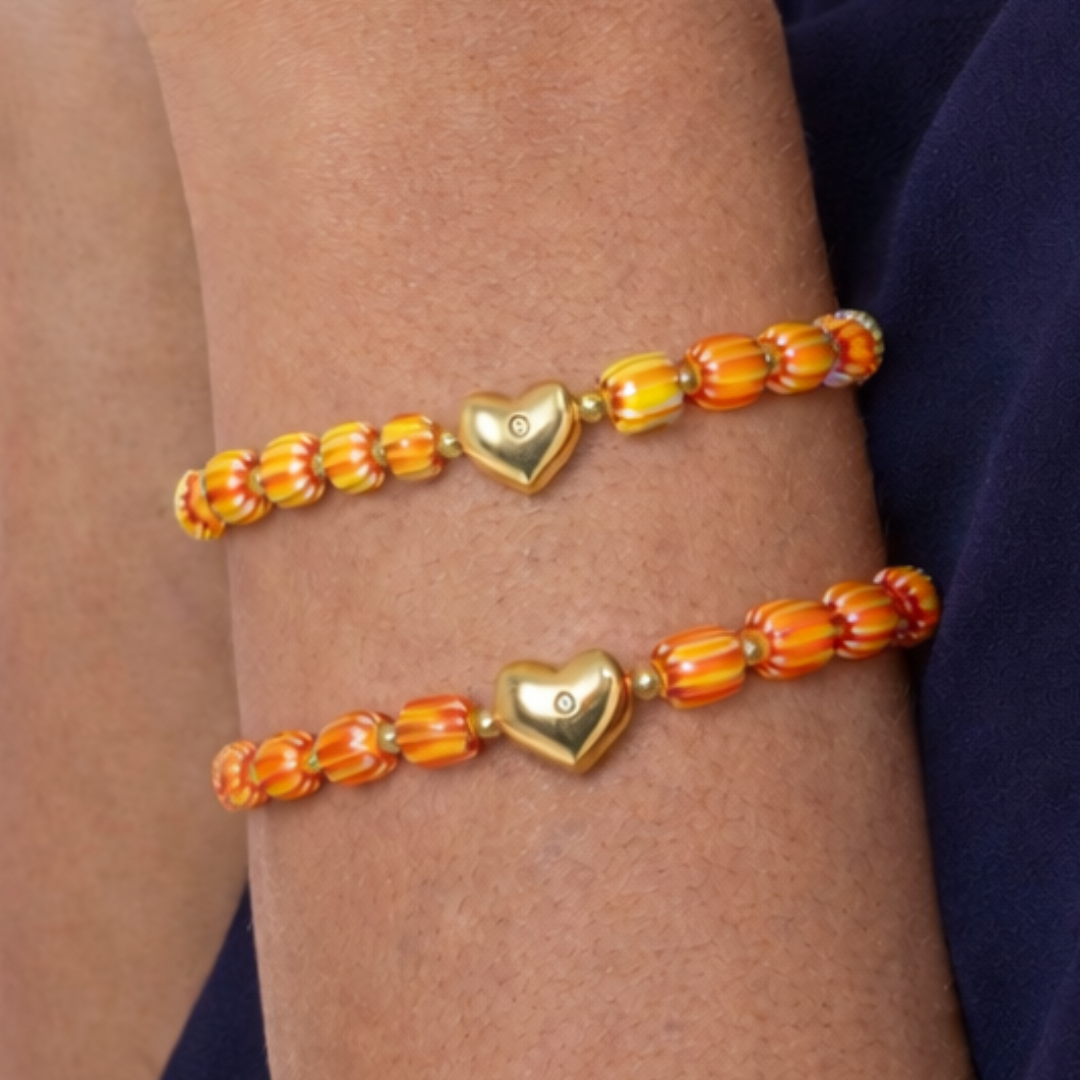 Geel-oranje gestreepte kralen armband met kleine 5 mm kralen en goudkleurig hartje, gedragen om de pols, Casa Jadel
