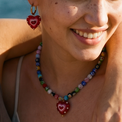 Model draagt set van kralenketting en oorbellen met grote glazen hart in rood.