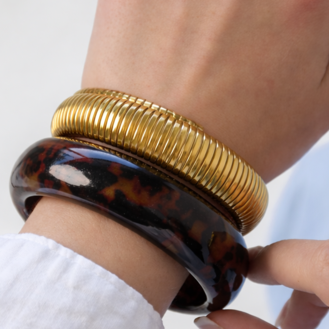 dames arm met gouden bangle en tortoise armband gecombineerd met statement ringen