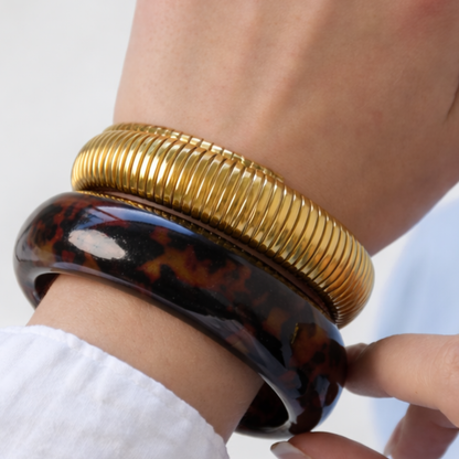 dames arm met gouden bangle en tortoise armband gecombineerd met statement ringen