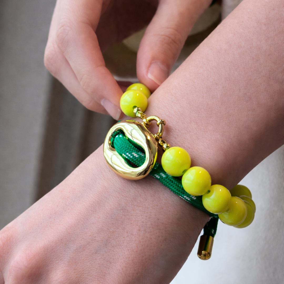Gouden bean armband met groene touwband en gele kralen, gedragen om de pols