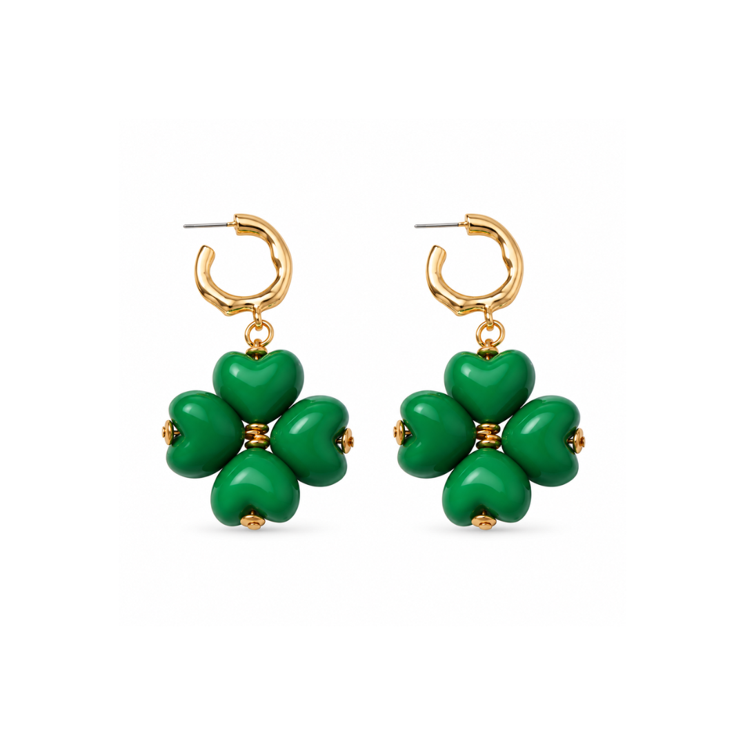 Gouden oorringetjes met een klavertje van vier glanzende groene hartjes en kleine goudkleurige kraaltjes op een witte achtergrond.