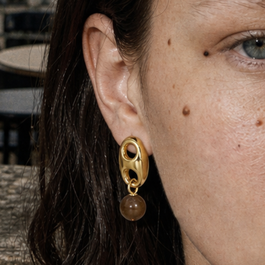 Model draagt gouden oorknopjes met bean hanger en bruine panterkraal | Casa Jadel