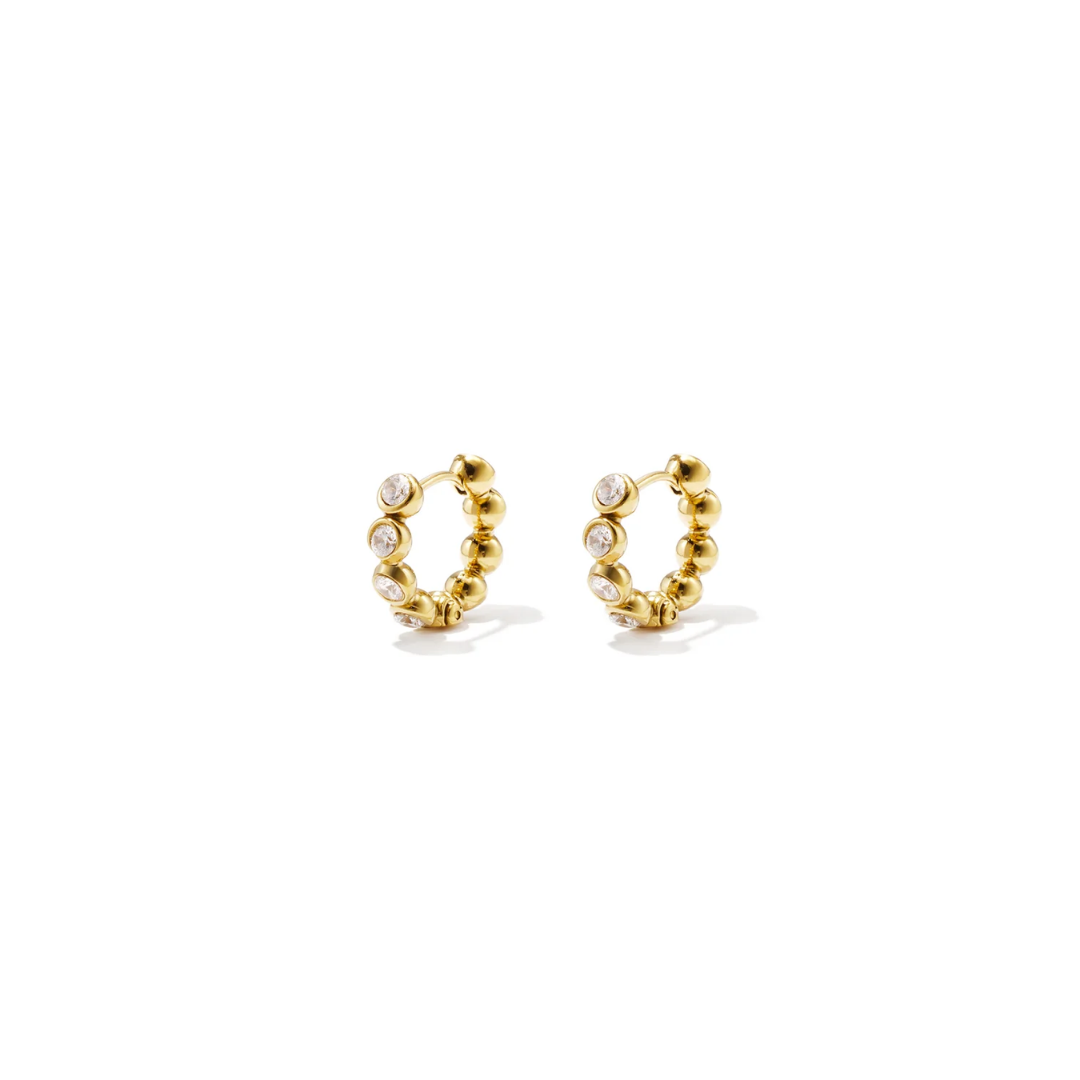 Kleine gouden oorringen met ronde gouden bolletjes en fonkelende heldere strass steentjes op een witte achtergrond