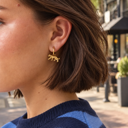model met Gouden oorringen met gedetailleerde panter bedels en goudkleurige kliksluiting op witte achtergrond