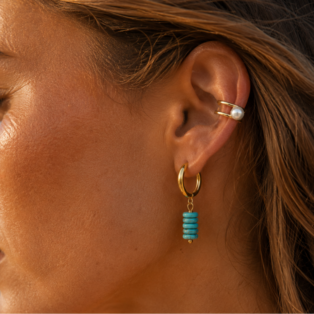 model met Gouden oorringen met turquoise natuursteen kralen en goudkleurige details 