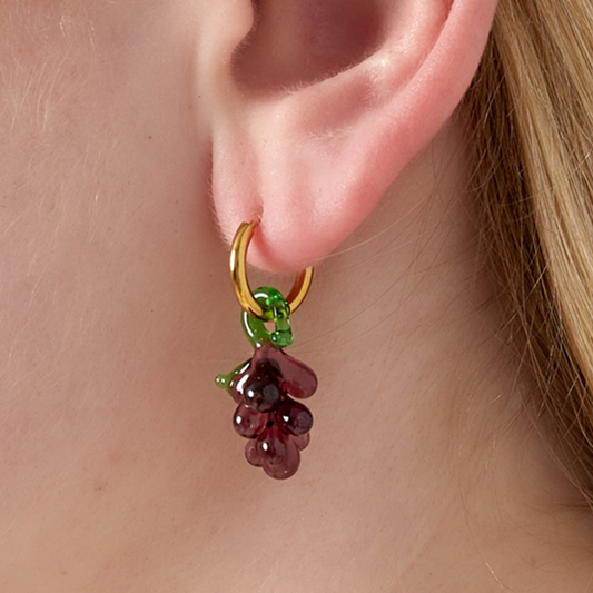 Gouden oorringetjes met paarse druiven hanger in glas gedragen aan oor.