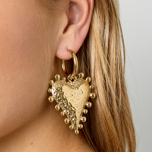 Gouden oorringetjes met statement hart en bolletjes detail gedragen door model.