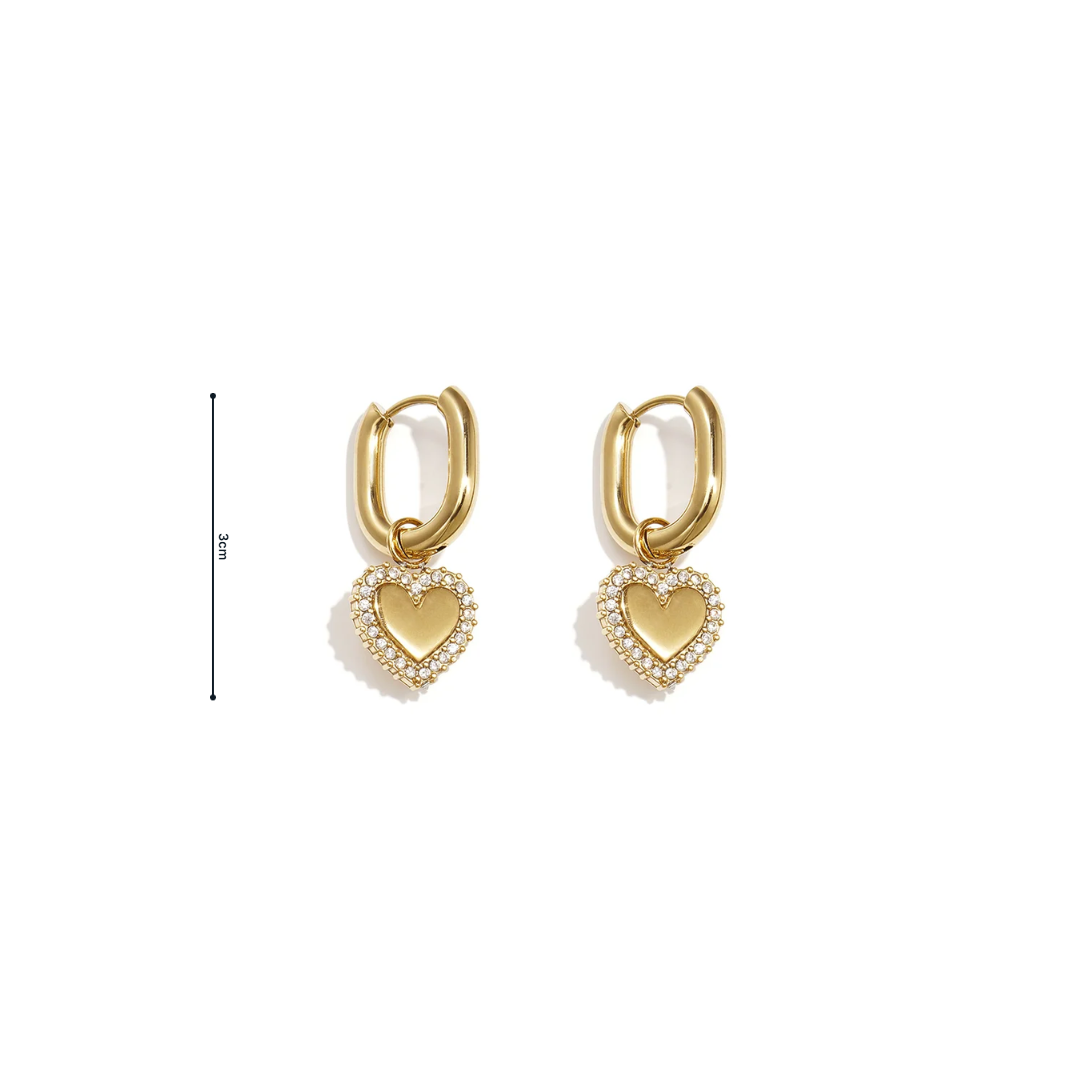 Gouden ovale oorbellen met hartvormige hanger en fonkelende strass steentjes op witte achtergrond afmeting