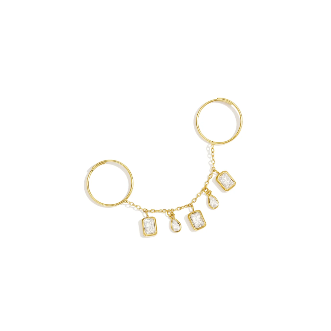 Gouden ring handchain met twee verbonden ringen en vijf hangende strass bedels, waarvan drie rechthoekig en twee druppelvormig, op een witte achtergrond.